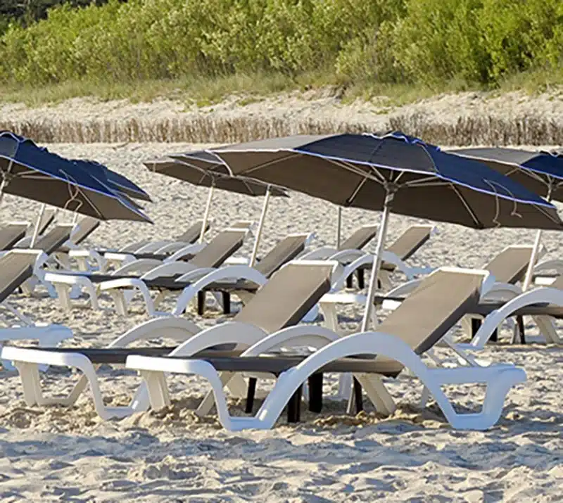 En la imagen se pueden observar unas 6-7 tumbonas de color gris con estructura blanca, en la playa.