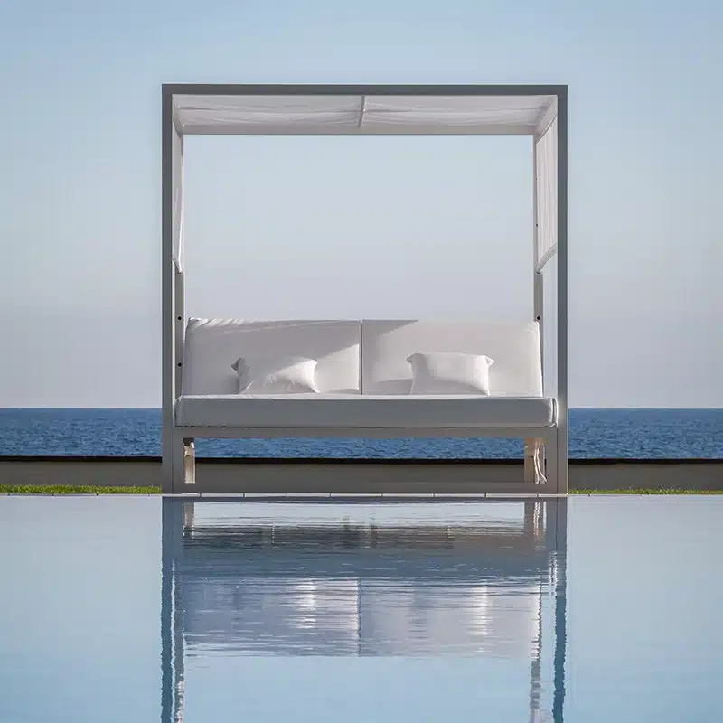 Cama balinesa moderna blanca con 2 colchónes individuales unidos de color blanco y almohadas a juego, diseño minimalista y elegante. Se ve de fondo el mar