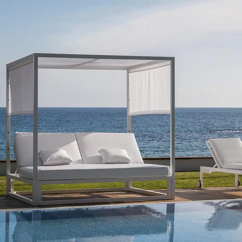 Cama balinesa moderna blanca con 2 colchónes individuales unidos de color blanco y almohadas a juego, diseño minimalista y elegante. Se ve de fondo el mar