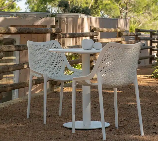 En la imagen se muestra dos sillas blanca sin reposabrazos con un diseño minimalista, las sillas estan junto a una mesa en una terraza